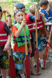 A line of children wearing life vests and holding rafting paddles