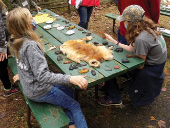 Kids sitting at a picnic table with an animal pelt in front of them