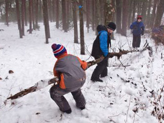A group of kids moving a log through the snow