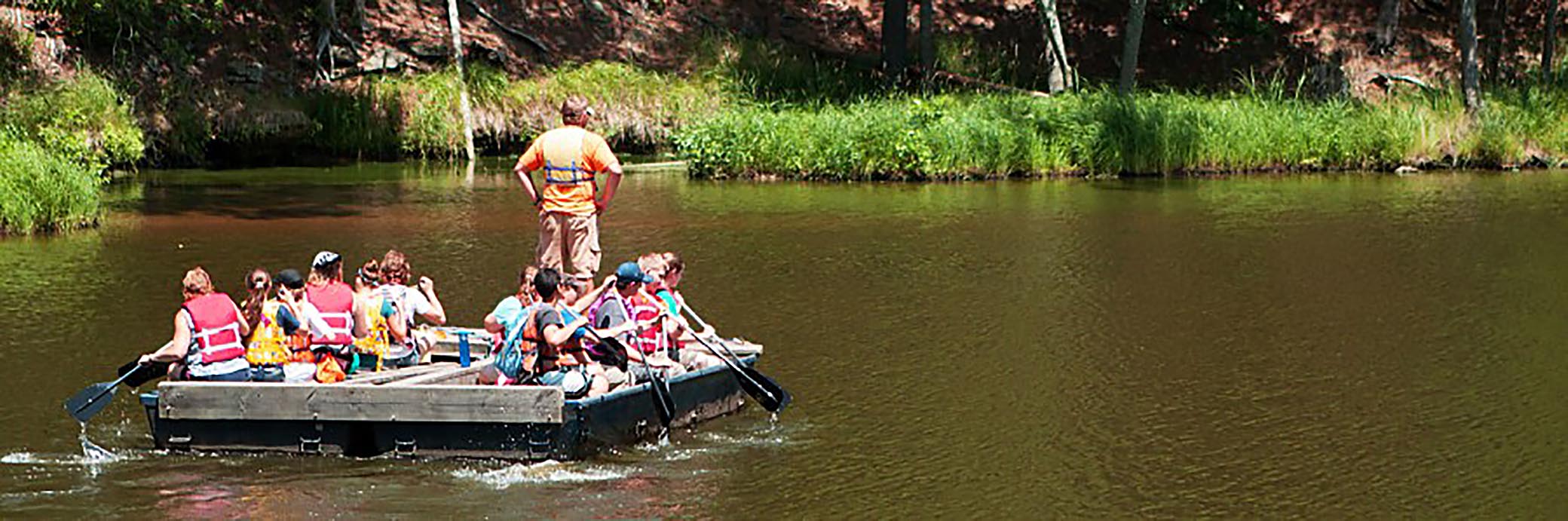 A group of 13 people on a large wooden raft in a river