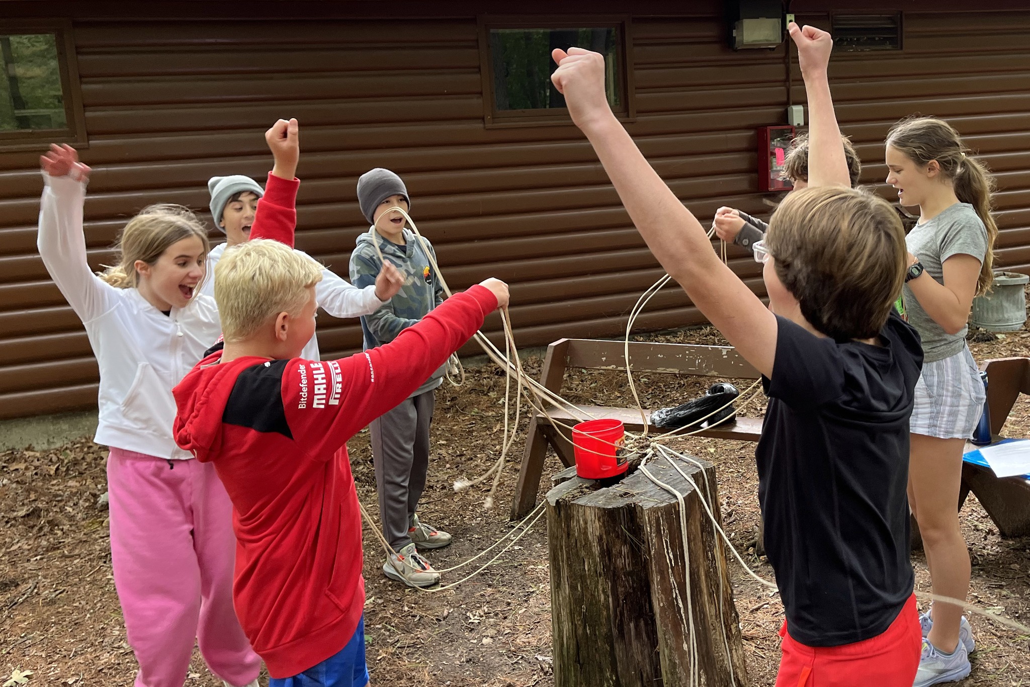 Group of youth standing around a stump with rope and hands in the air, celebrating