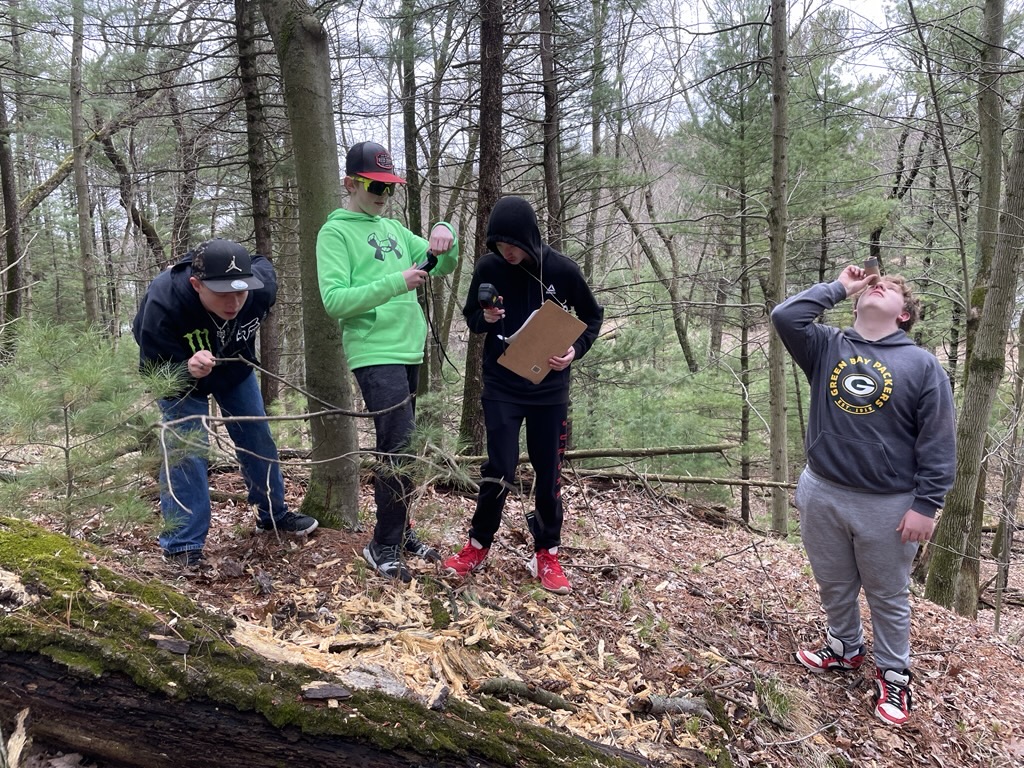 Four middle school students use hand held tools to take microclimate data in a forest