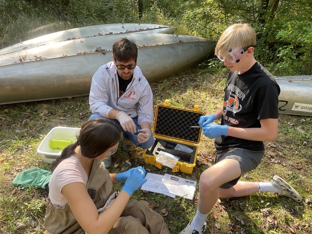 1 adult and 2 high school youth, 1 in waders, test a water sample using a kit
