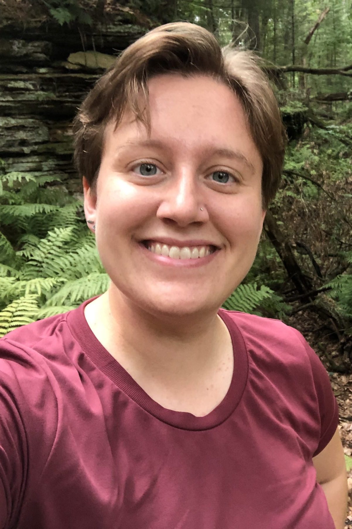 A woman with short hair wearing a maroon shirt with a dark vest