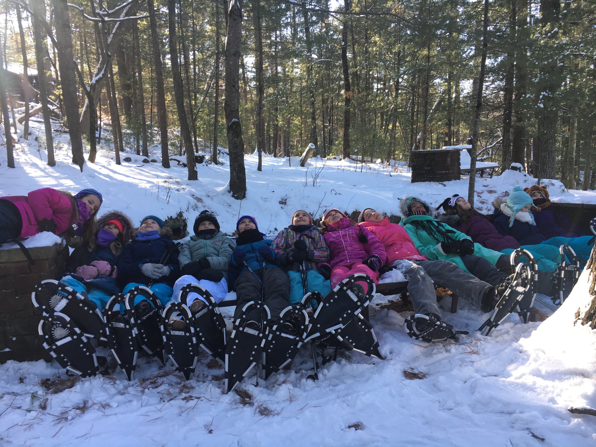 Large group of snowshoeing youth laying on benches